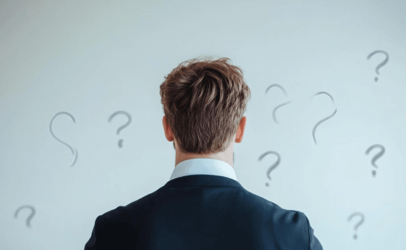 Man in a suit standing with his back turned facing a wall covered in question marks, symbolizing uncertainty and the process of transforming self-doubt into meaningful lessons