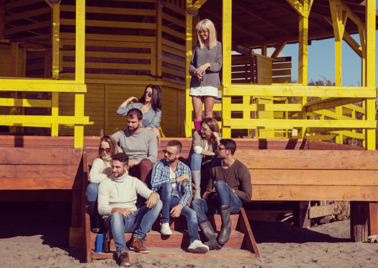 Diverse group of friends laughing and connecting together outdoors on wooden bleachers in the sunshine, representing the journey from isolation to authentic community and belonging